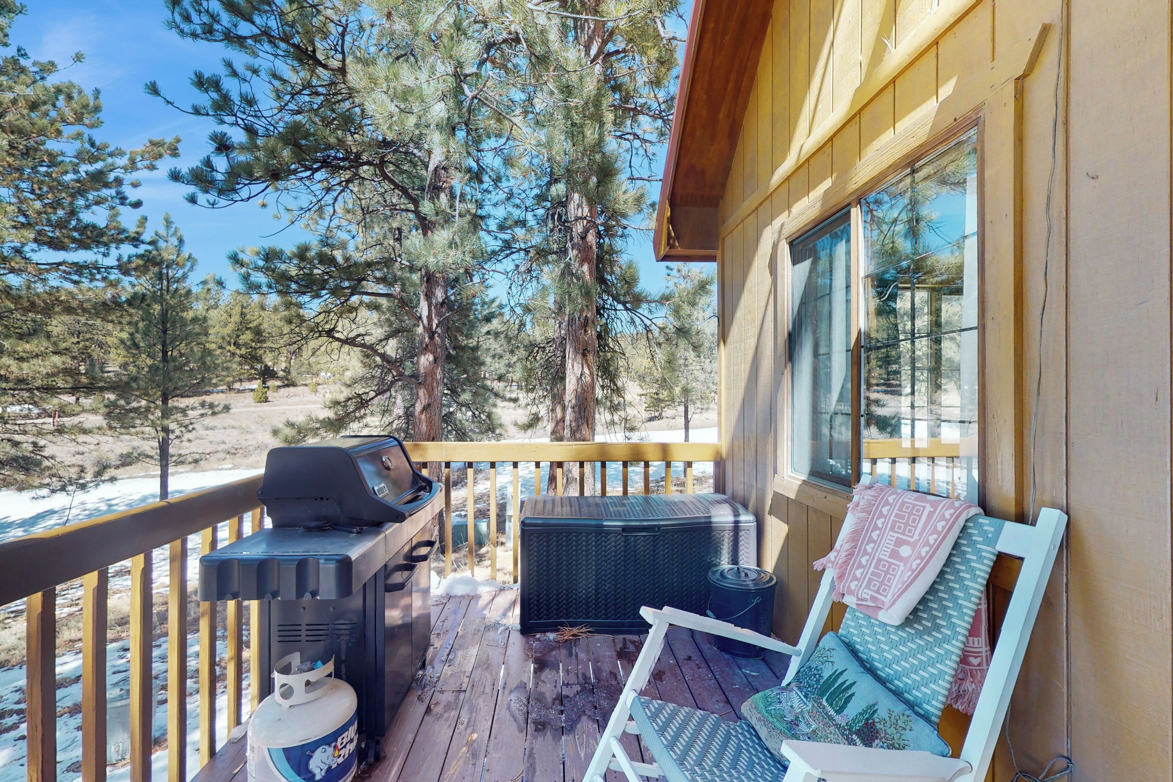 A wooden deck with a grill, a large cooler, and a lounge chair with a patterned cushion.