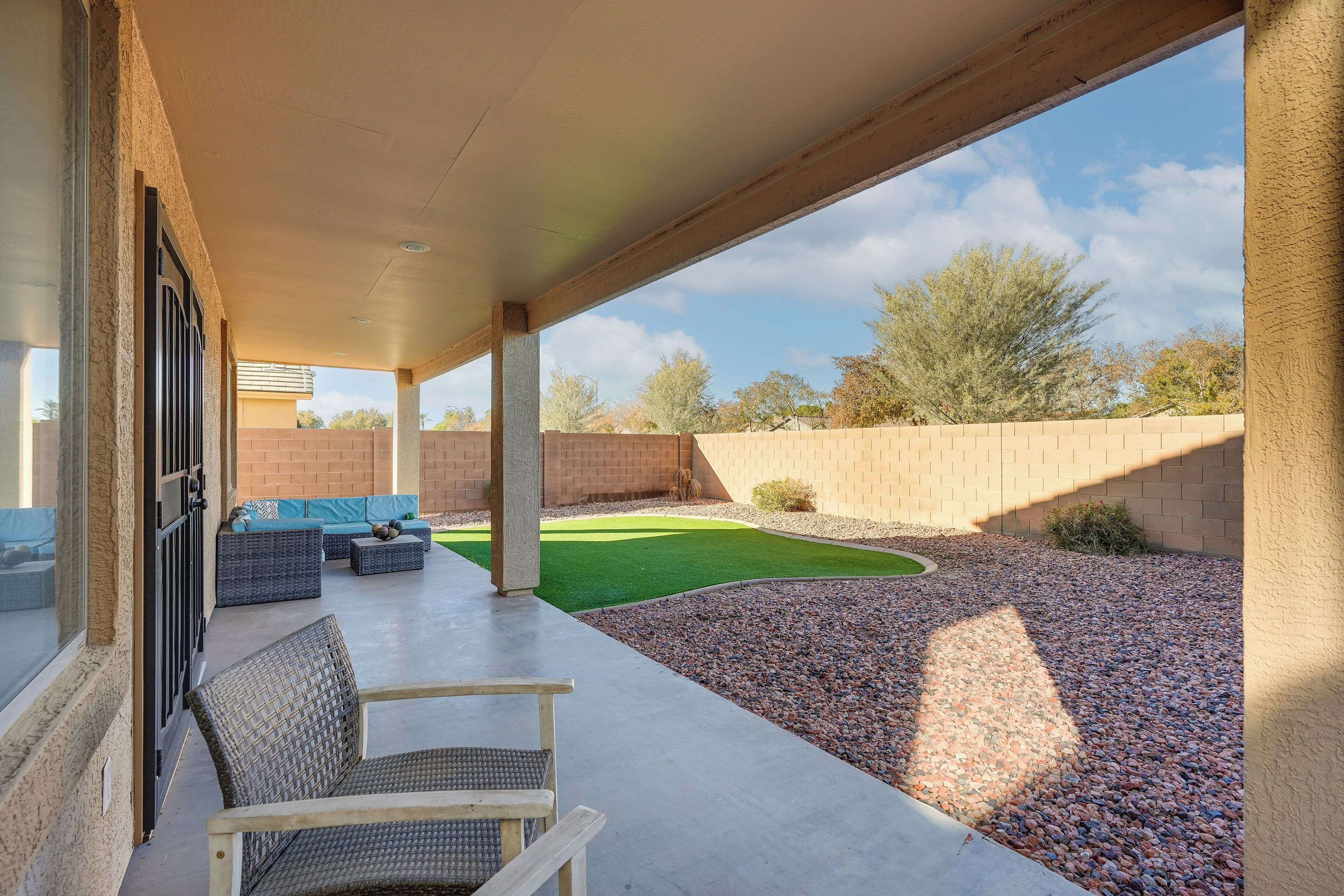 A covered patio with outdoor seating, a small lawn, and a view of the surrounding landscape.