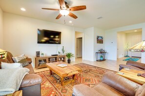 A spacious living room with a ceiling fan, a flat-screen TV mounted on the wall, a wooden coffee table, leather sofas, and a patterned rug. - Outdoor Oasis & Amenity Access: Buckeye Retreat (Buckeye)