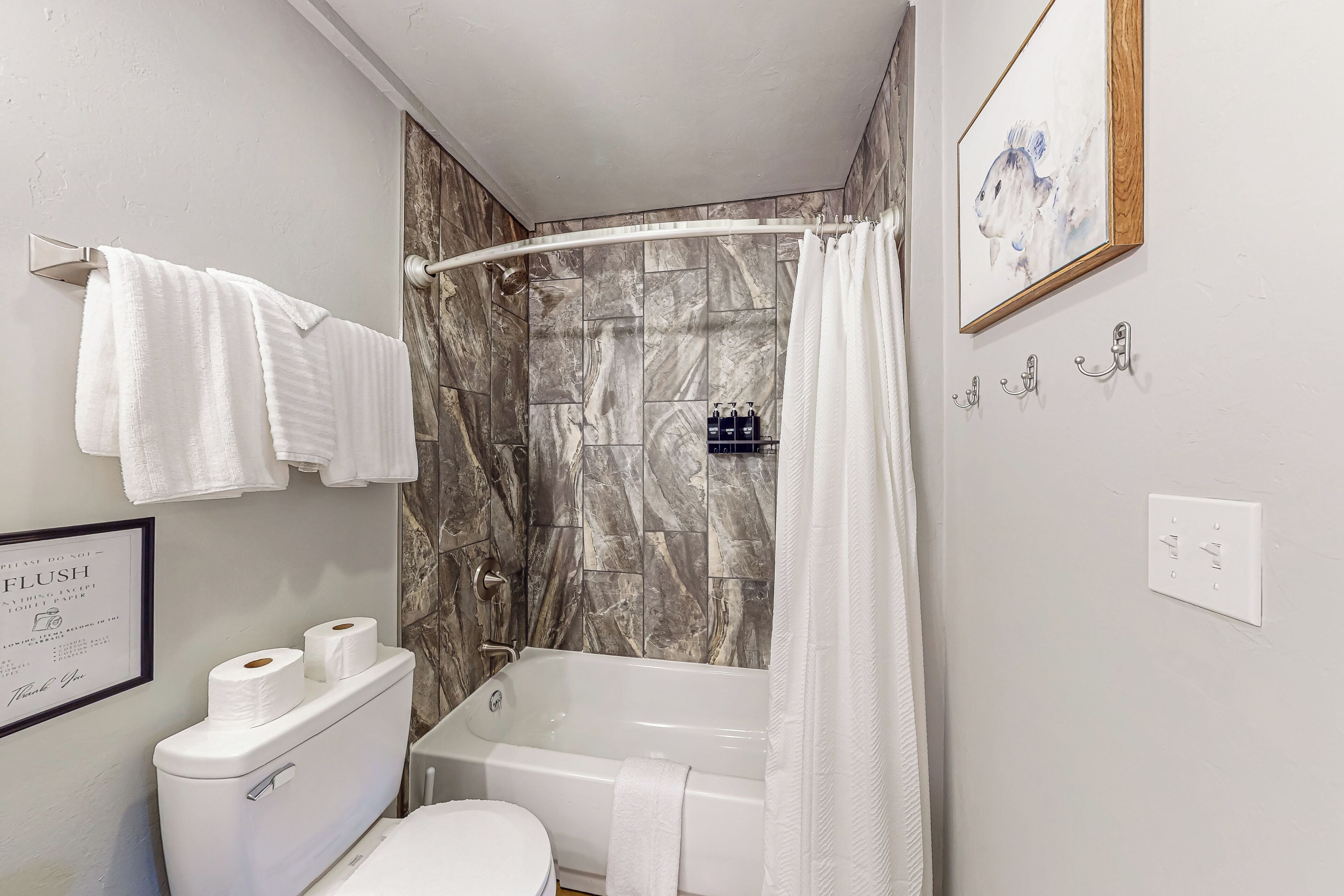 Een badkamer met douche, toilet en bad. Handdoeken hangen aan een rek, en een lijst met tekst hangt aan de muur.
