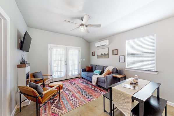 Un salon comprenant un canapé, des fauteuils, une table basse, un ventilateur de plafond et une grande fenêtre avec des stores.