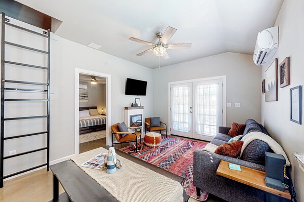 A modern living room with a sofa, chairs, a coffee table, a TV, and a ceiling fan. - Steps to Lake Eufaula: Home w/ Fire Pit & BBQ (Eufaula)
