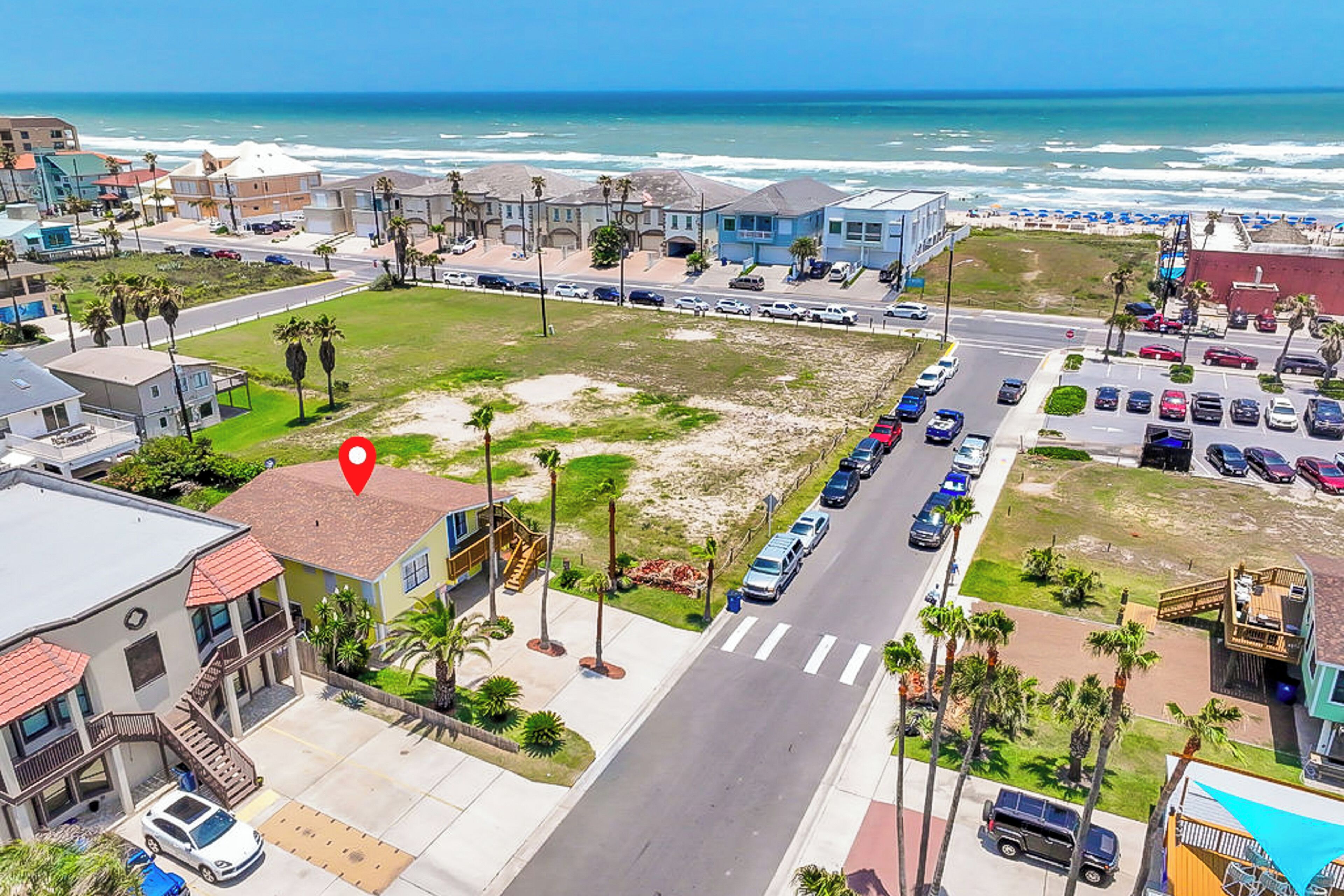 Un quartier résidentiel situé sur la côte, offrant une vue sur la plage, avec un parking et une route menant à la plage.