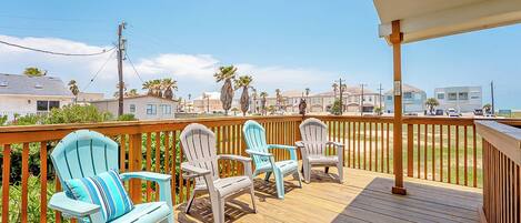 A wooden deck with three Adirondack chairs and a covered area.