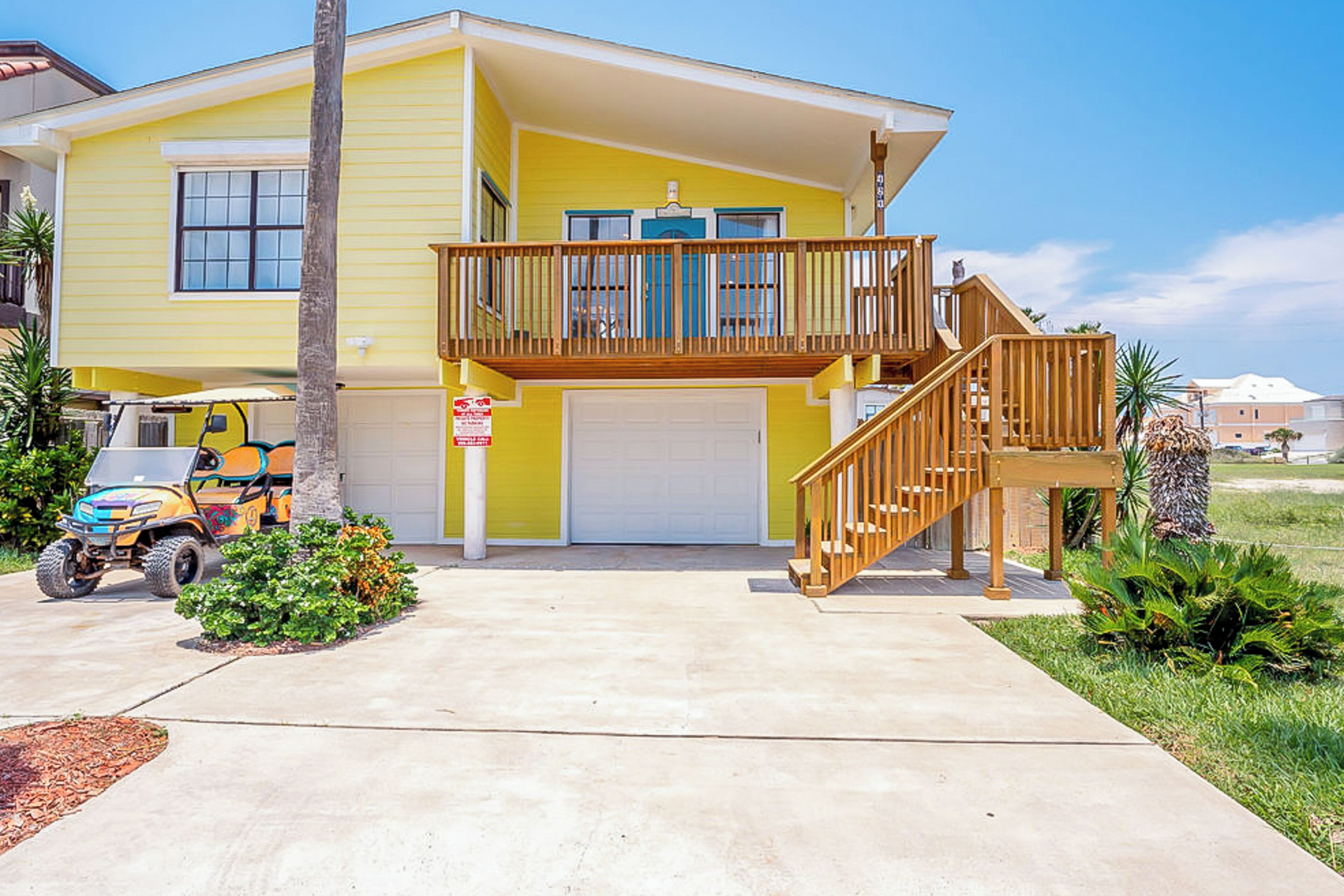 A two-story yellow house with a wooden balcony and a garage.