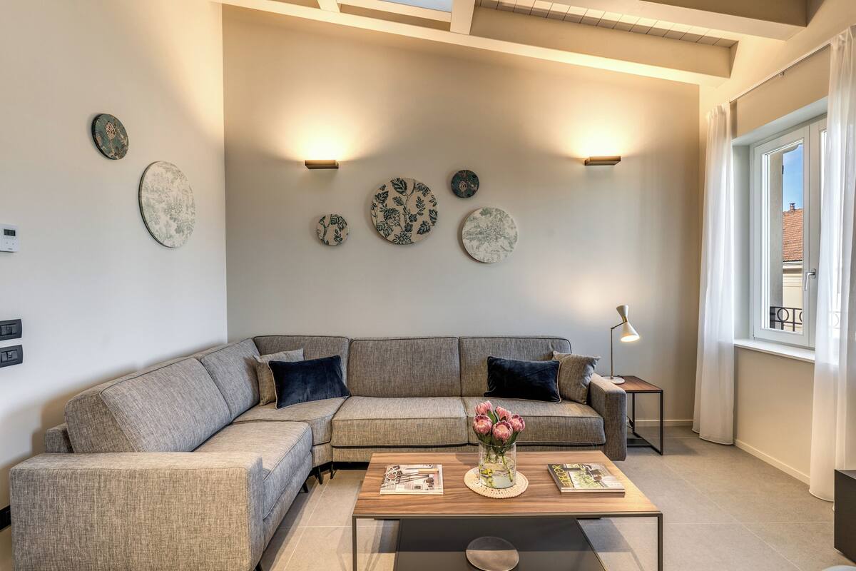 A modern living room with a sectional sofa, a coffee table with magazines, wall-mounted decorative plates, and a floor lamp.