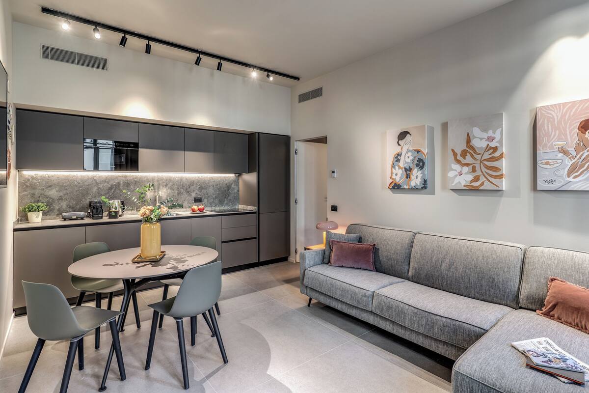 A modern kitchen with dark cabinets, a marble countertop, and a dining area with a round table and chairs.
