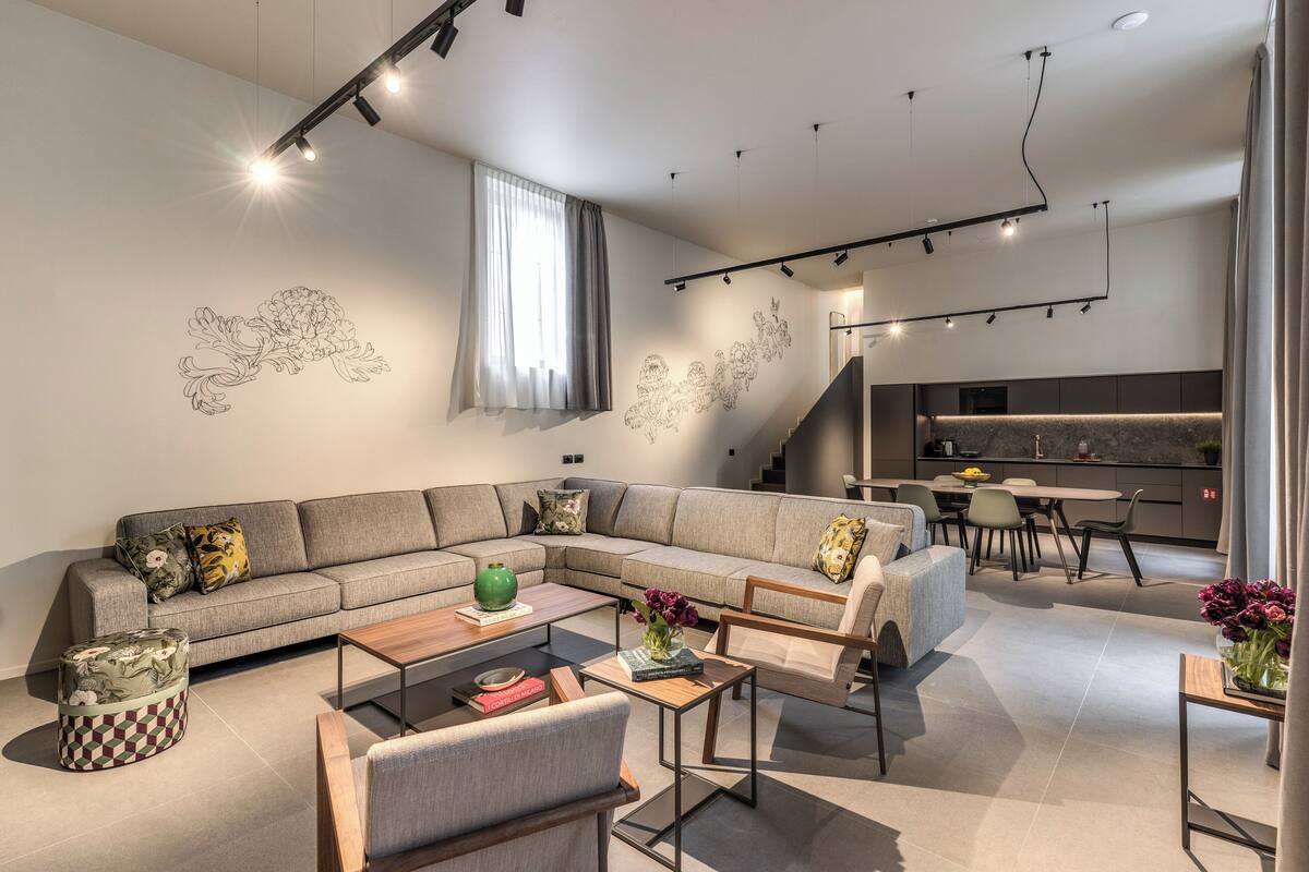 A modern living room with a sectional sofa, a coffee table, and a dining area with a kitchen in the background.