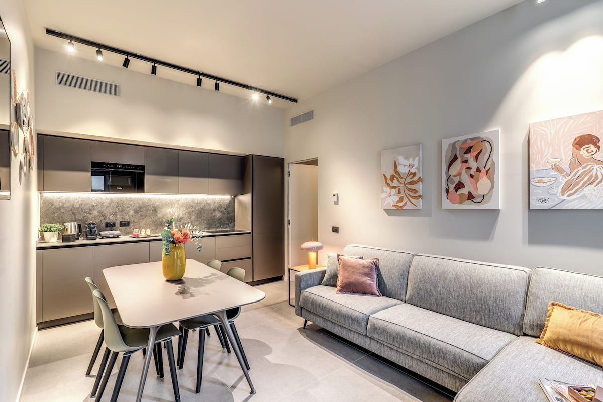 A modern kitchen with a dining area, a sofa, and artwork on the walls.