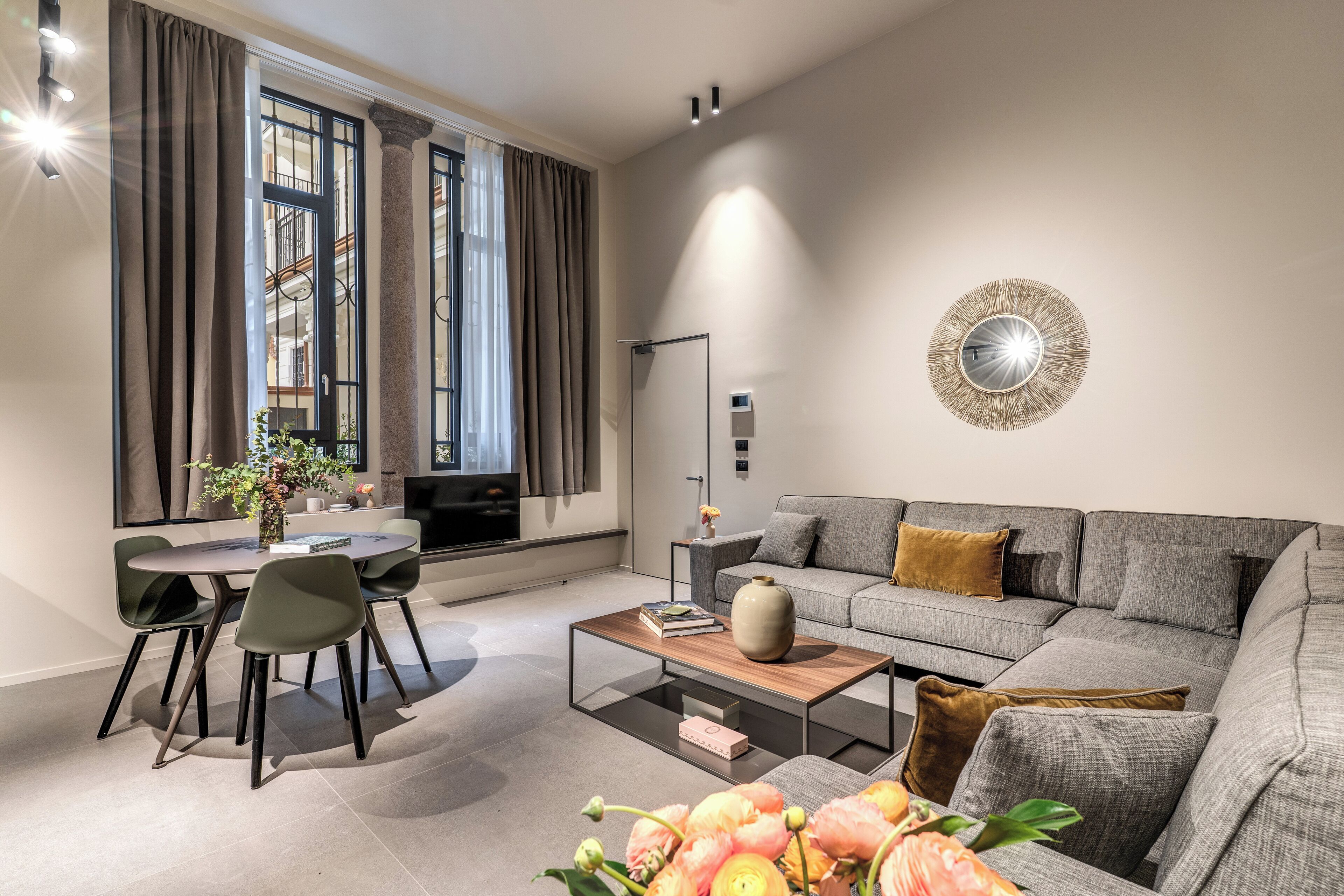 A modern living room with a grey sofa, a coffee table, and a dining area with chairs.