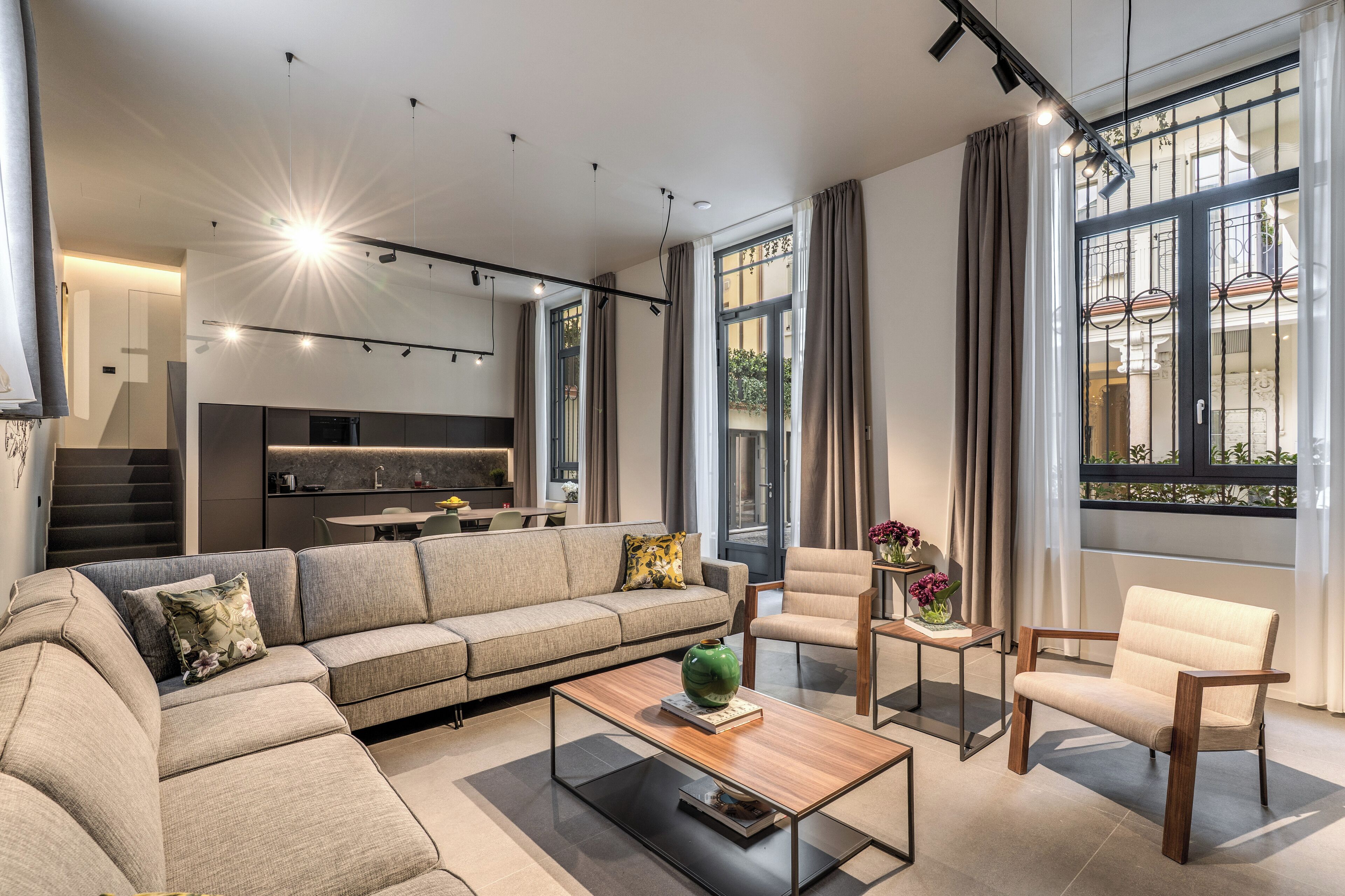 Un salon moderne avec un canapé, des fauteuils, une table basse et une cuisine en arrière-plan.