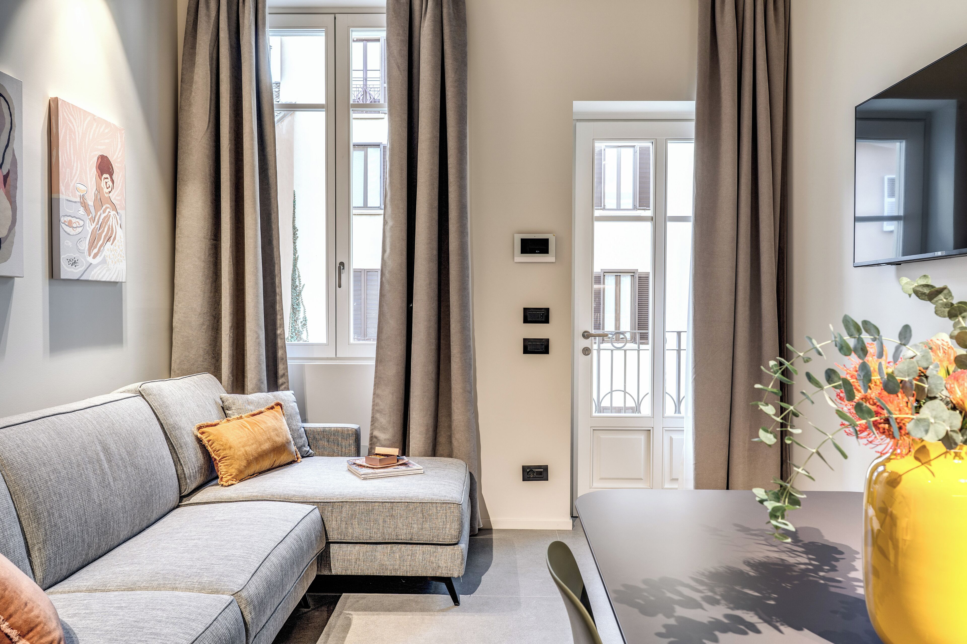 Un salón moderno con un sofá gris, una mesita y un jarrón amarillo con flores.