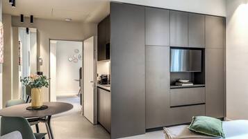 Een moderne keuken met inbouwapparatuur, een eethoek met een ronde tafel en een woonruimte met een bank en een groen kussen.