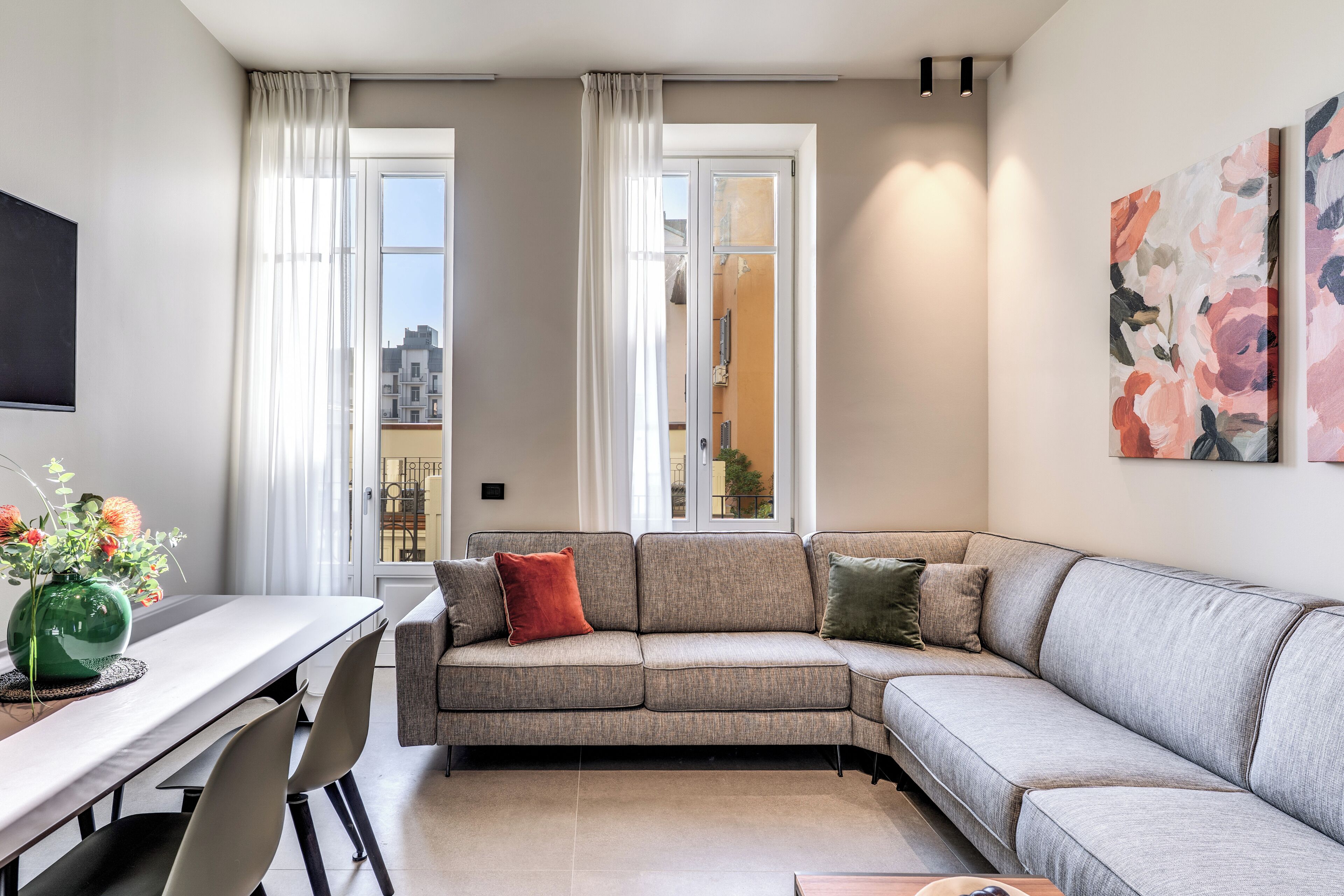 Una sala de estar moderna con un sofá seccional gris, una mesa de comedor con sillas y un ventanal con cortinas.