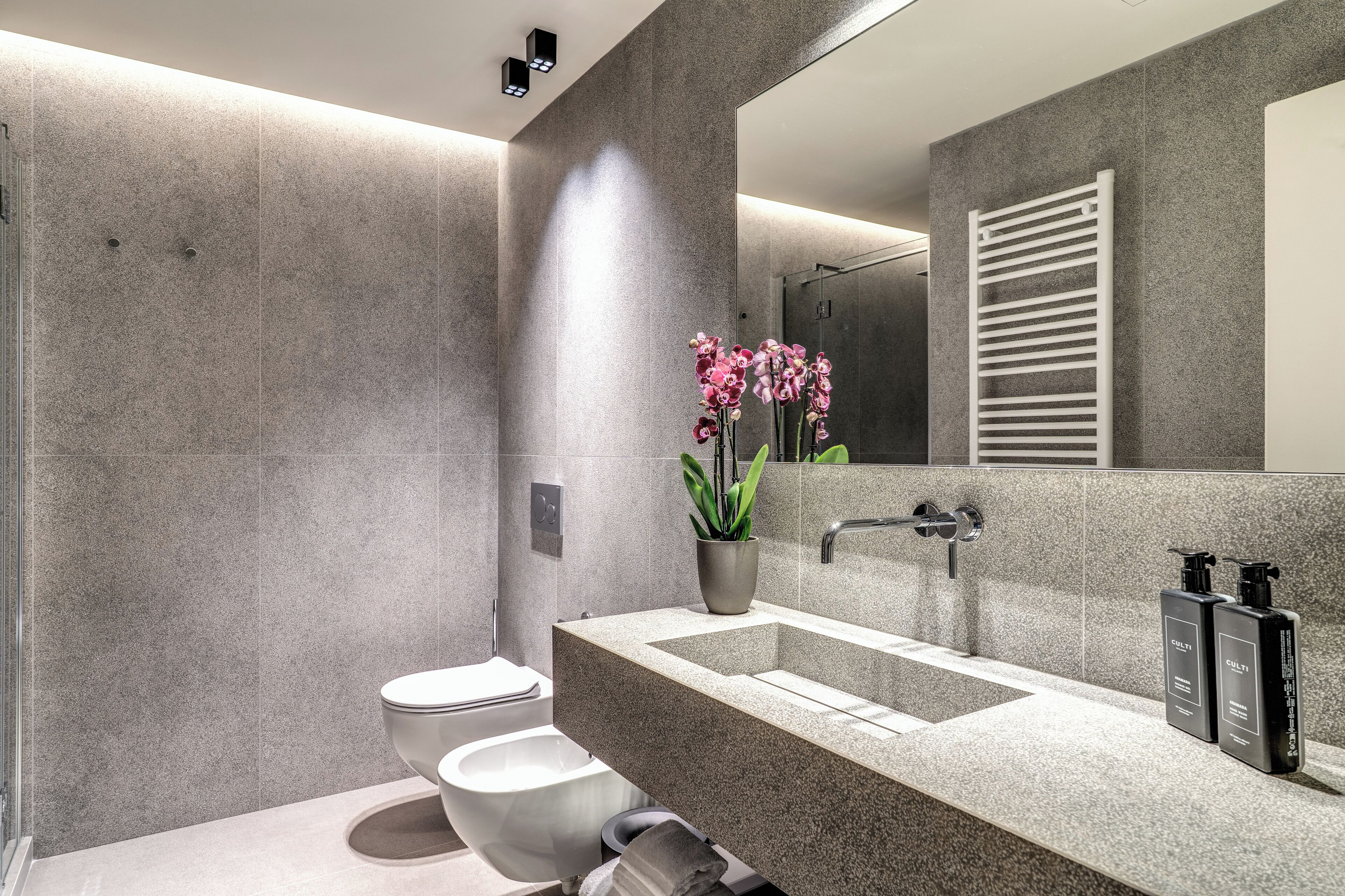 A modern bathroom with a large mirror, a sink, and a toilet.