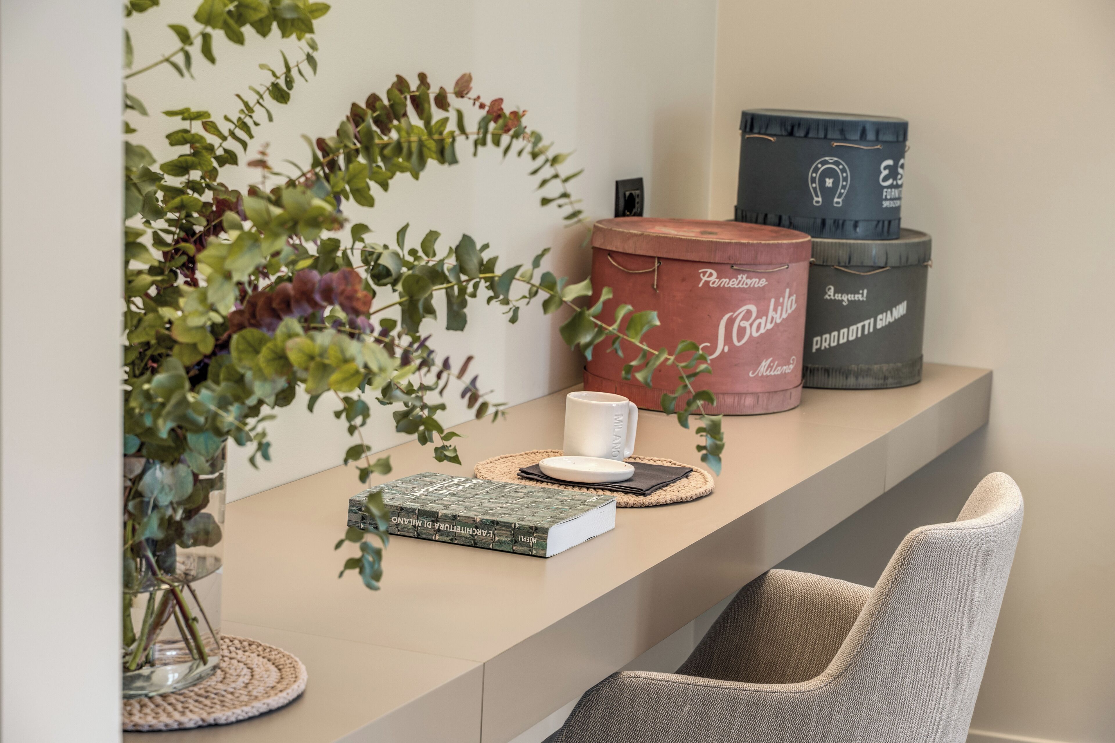 A modern interior with a beige countertop, a woven placemat, a book, a white mug, and decorative containers.