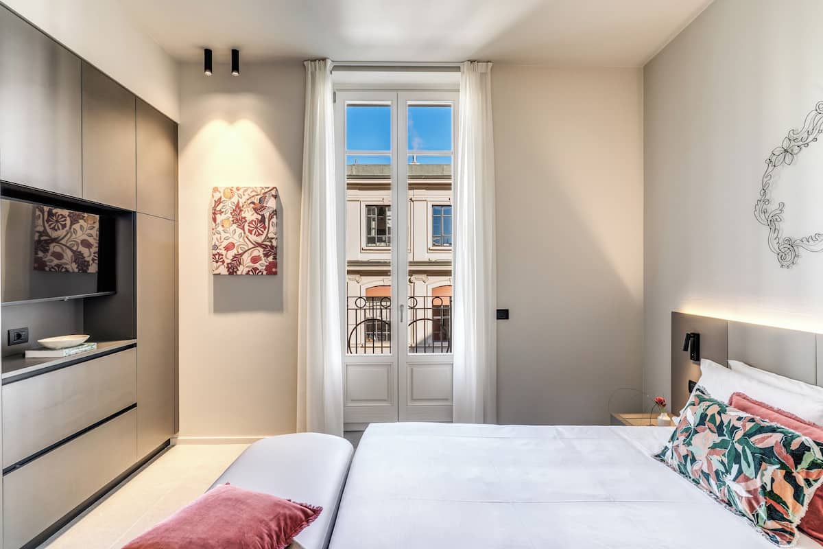 A modern bedroom with a bed, bedside table, and a view of the outside through a glass door.