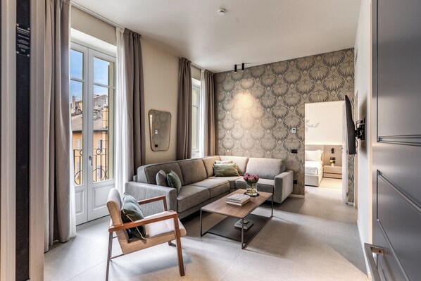 A modern living room with a sofa, coffee table, and a chair. There is a patterned wallpaper on the wall and a window with curtains. - Seety Spartaco (Milan)