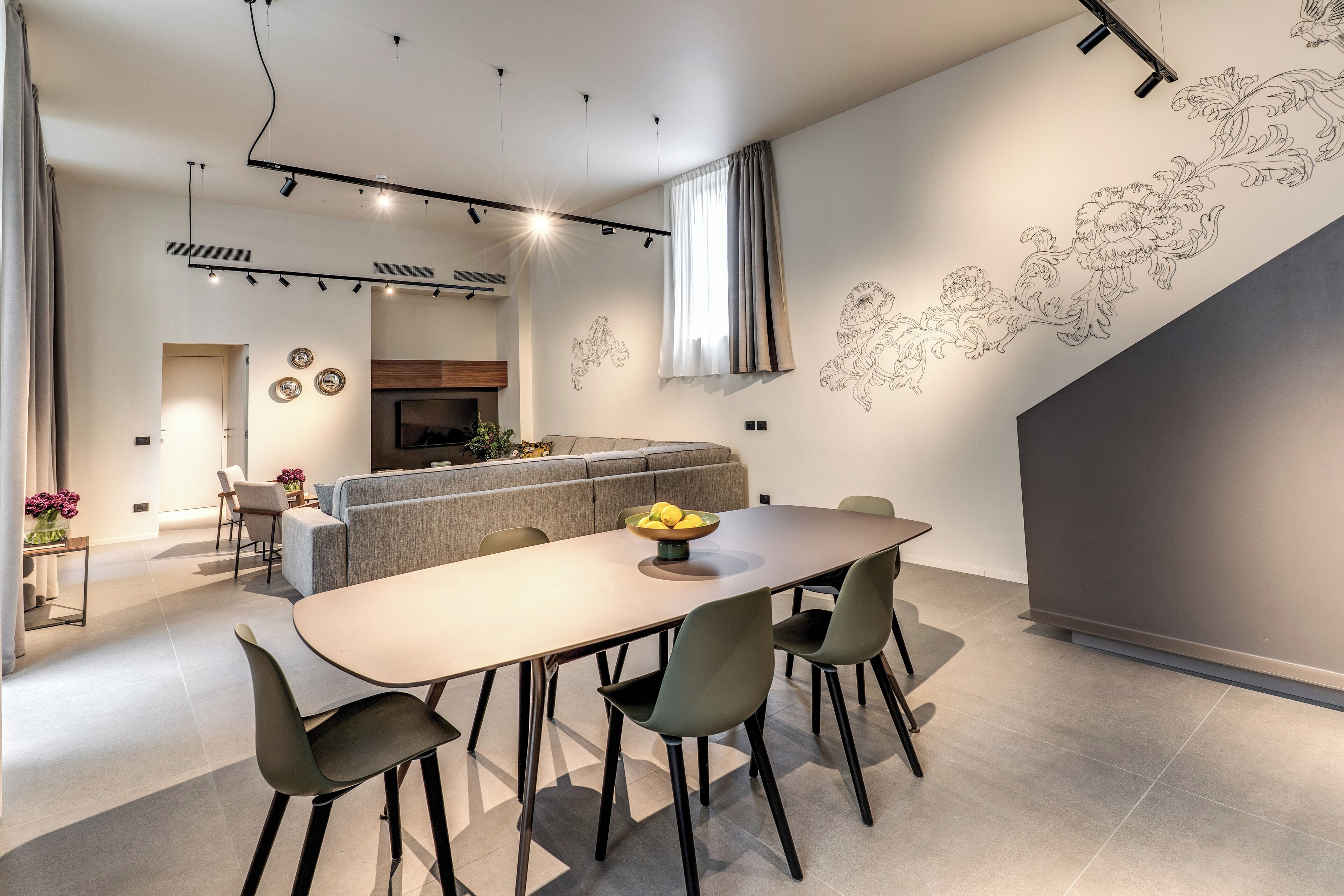 A modern kitchen with a dining area, featuring a long table, four chairs, and a central island with a bowl of lemons.