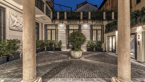 A courtyard with cobblestone flooring, stone columns, and potted plants. - Seety Spartaco (Milan)