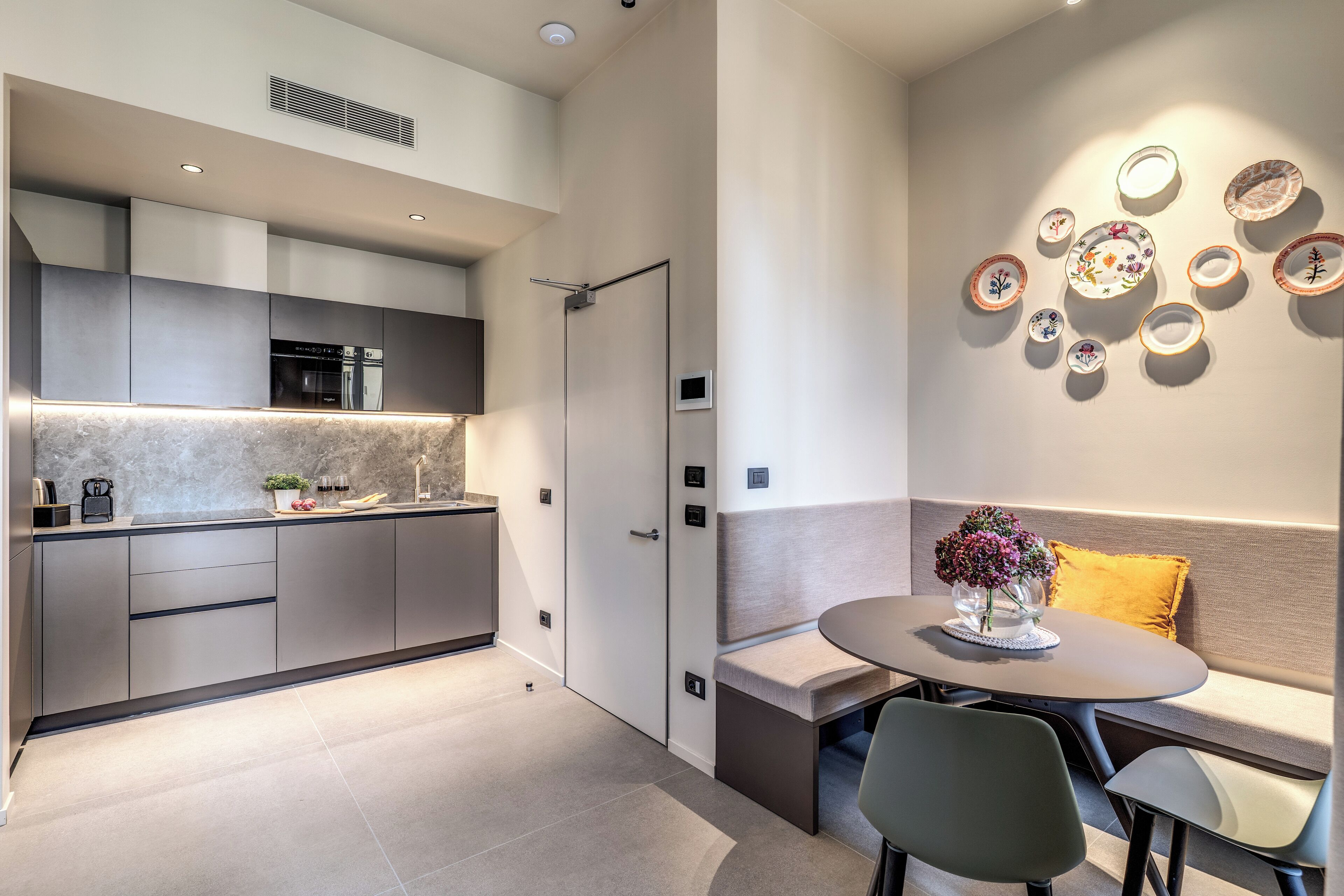 A modern kitchen with grey cabinetry, a built-in oven, and a dining area with a round table and chairs.