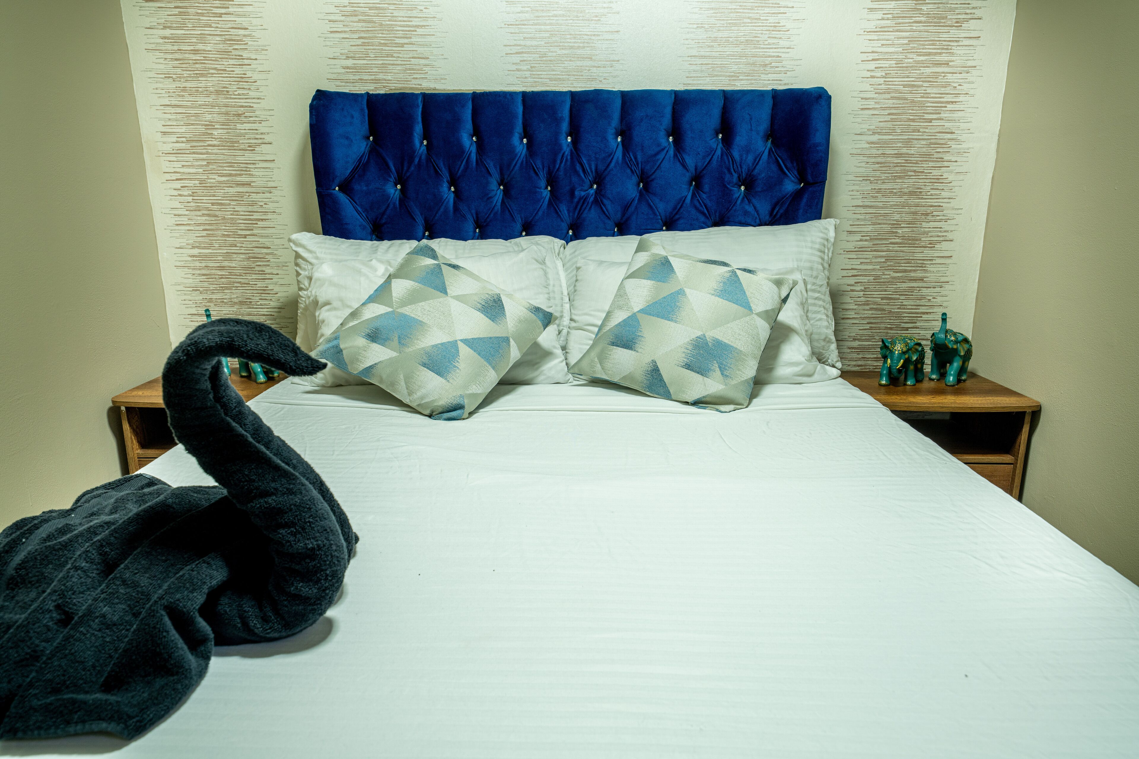 A bed with a tufted headboard, two pillows with geometric patterns, and a dark-colored bathrobe on the bed.