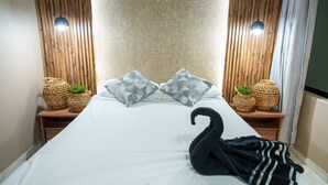 Una cama bien hecha con dos almohadas, una toalla negra y dos cestas tejidas con plantas a cada lado.