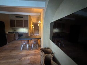 Moderni keittiö, jossa on puiset kaapit, ruokapöytä tuoleineen ja suuri ikkuna.