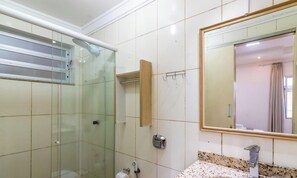 Une salle de bain avec une douche à parois de verre, une étagère en bois, un miroir et un comptoir en granit.