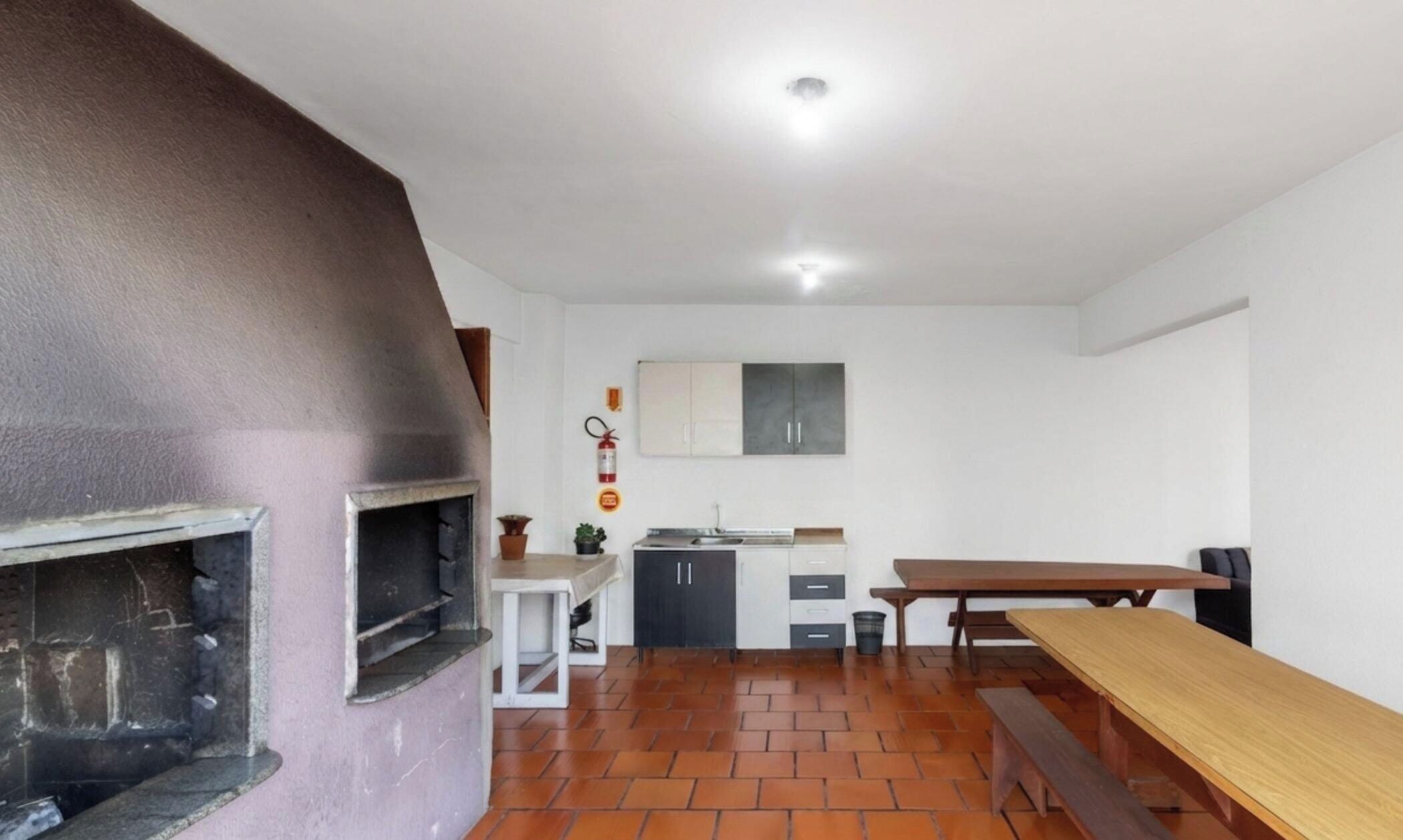 Uma cozinha com piso de tijolos, mesa de madeira, um banco e um armário branco.