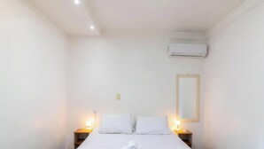 Une chambre d’hôtel avec un lit, des lampes de chevet, un climatiseur et un miroir au mur.