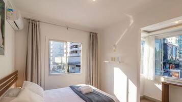 Quarto de hotel com cama, janela com cortinas, ar condicionado fixado na parede e vista para edifícios lá fora.