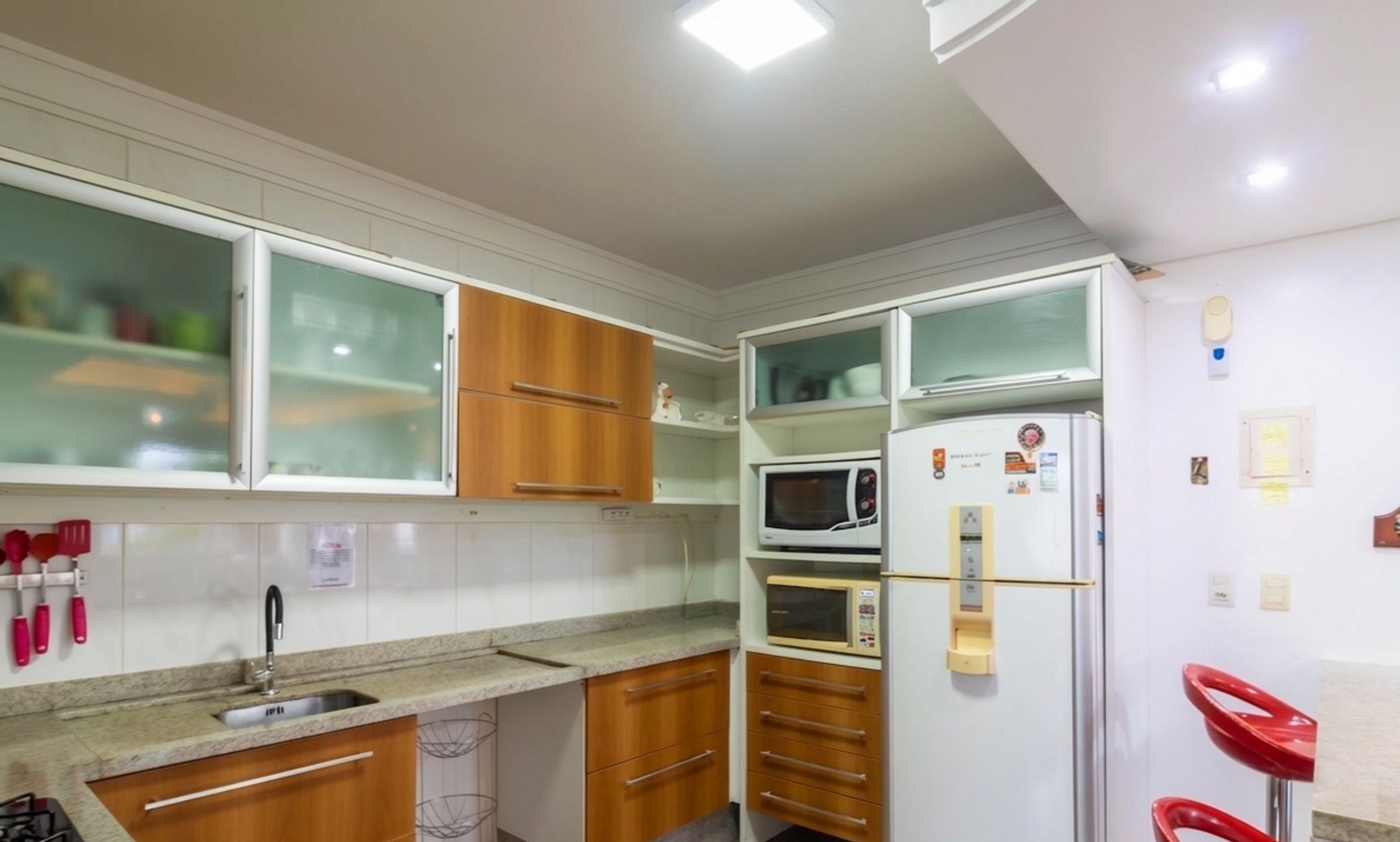 A compact kitchen with wooden cabinets, a microwave, a refrigerator, and a sink.