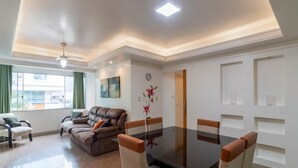 Un salon moderne comprenant un canapé, une table à manger avec des chaises, un luminaire au plafond et une fenêtre avec des rideaux.