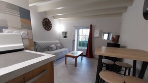 Una cocina moderna con horno integrado, un comedor con mesa de madera y taburetes de bar, y una sala de estar con sofá y un reloj en la pared.