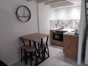 A compact kitchen with a wooden table and stools, a built-in oven, and a tiled backsplash. - Chez Lilian & Isa - Gîte 4 people (Pouzauges)