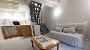 Una sala moderna con un sofá, una mesa de centro de madera y una zona de cocina con microondas y armarios.