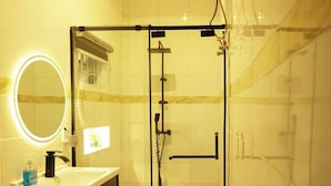 Ein modernes Badezimmer mit einer gläsernen Dusche, einem Waschtisch mit Spiegel und Seifenspender sowie einer Leuchte über dem Spiegel.