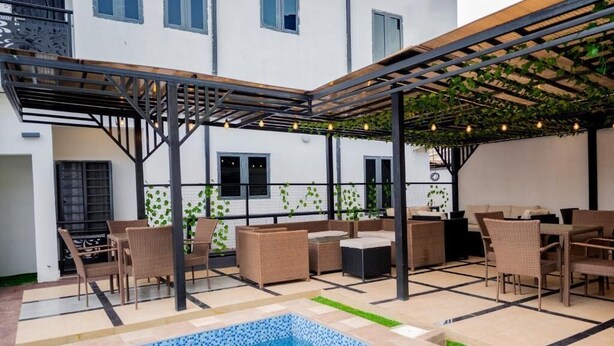 Ein Poolbereich im Freien mit einer Pergola, Sitzgelegenheiten und einer gefliesten Terrasse.