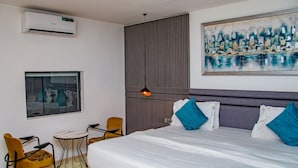 Ein modernes Hotelzimmer mit einem großen Bett, einem kleinen Tisch mit zwei Stühlen, einem Fenster, einer Klimaanlage und einem Stadtbild an der Wand.