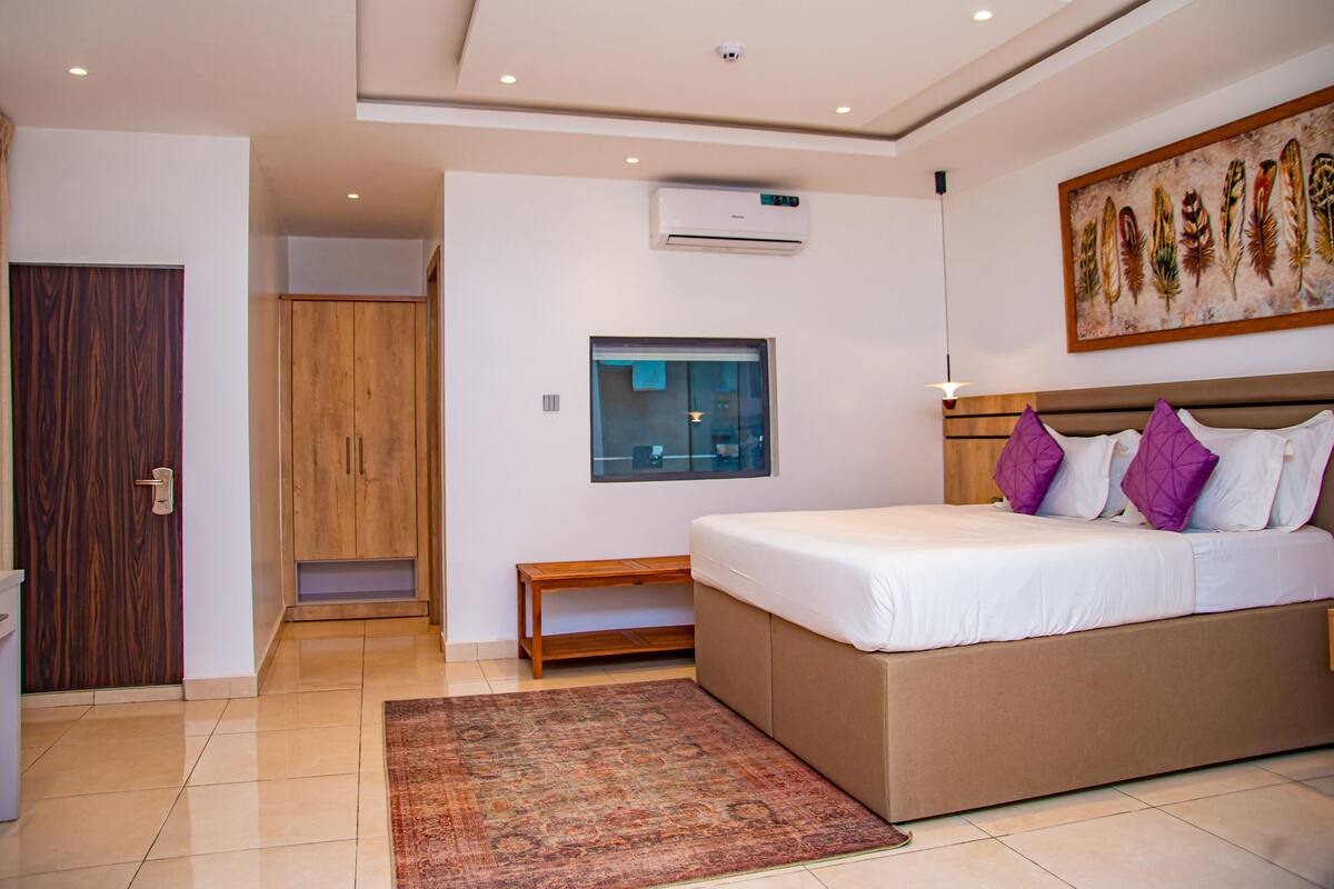 Un dormitorio moderno con una cama grande, un armario de madera, una mesita pequeña y una lámpara del techo.