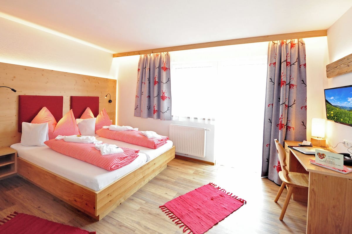 A bedroom with a wooden bed, red and white checkered bedding, a desk with a computer, and a window with curtains.