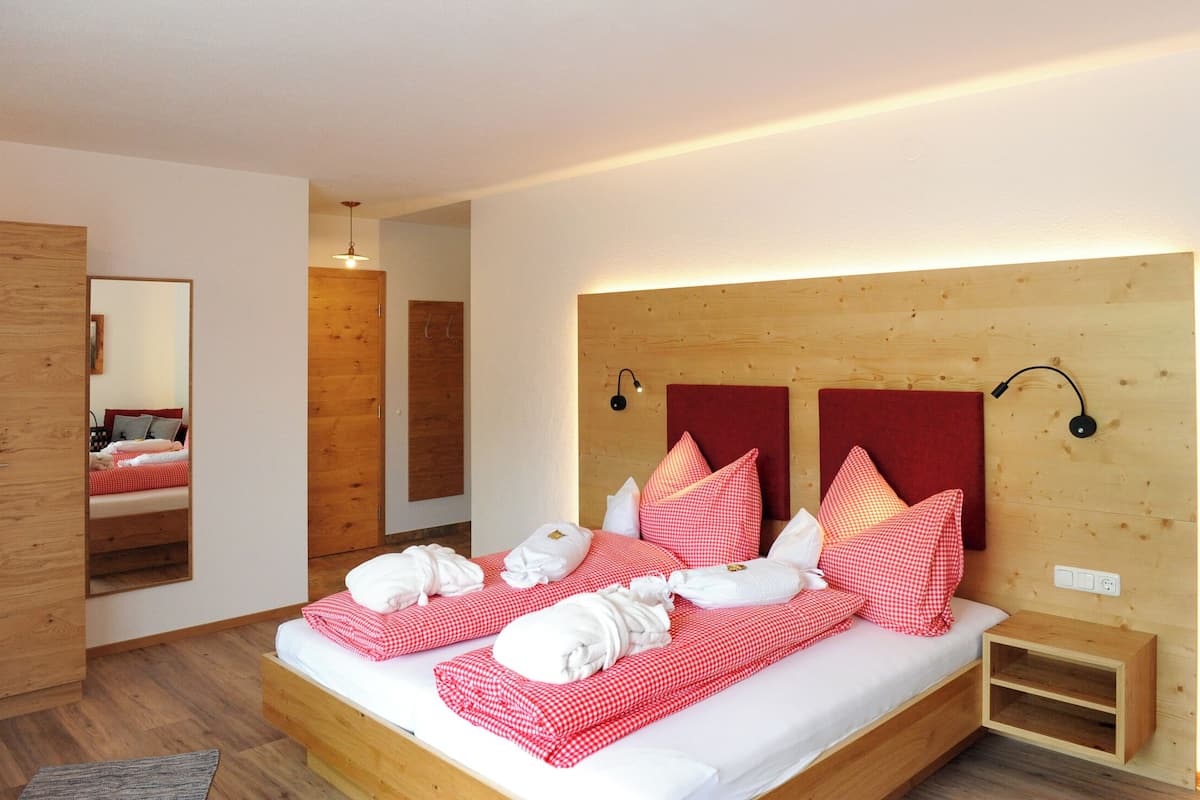 A neatly made double bed with red and white checkered bedding, a wooden headboard, and a bedside table with a lamp.
