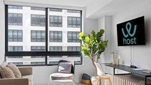 Ein modernes Wohnzimmer mit großem Fenster, Flachbildfernseher, Schreibtisch und gemütlicher Sitzecke.