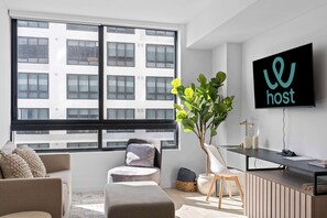 A modern living room with a large window, a flat-screen TV, a desk, and a comfortable seating area. - 1BR· walk to FIFA Fan Fest ·Pool Deck & Co-Working (Miami)