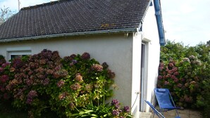 A house with a tiled roof, a garden with hydrangeas, and a blue folding chair. - "Chestnut, between land and sea (Plouézec)