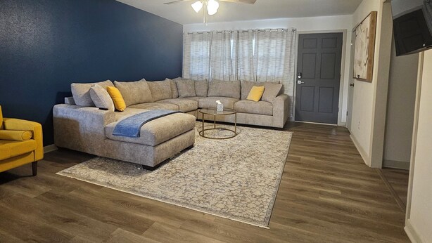 A living room with a sectional sofa, a yellow armchair, a round coffee table, and a ceiling fan. - Medical Oasis - 2 Kings, 1 Queen - Work desk (Lubbock)