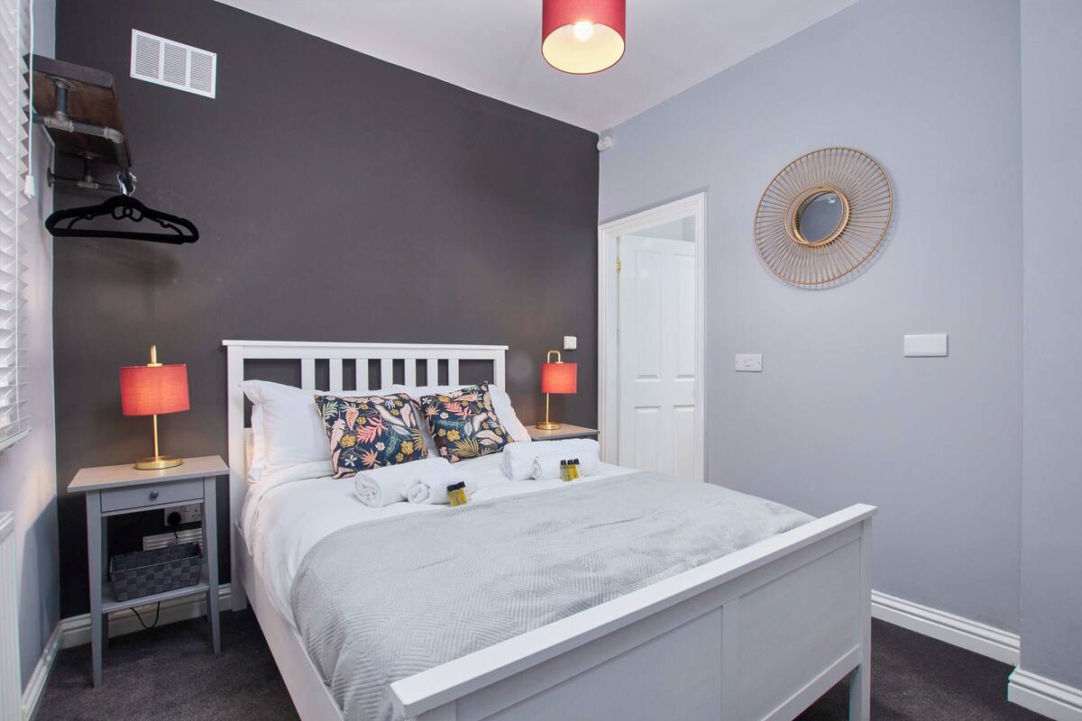 A neatly arranged bedroom with a bed, two bedside tables, a hanging light fixture, a mirror, and a door.