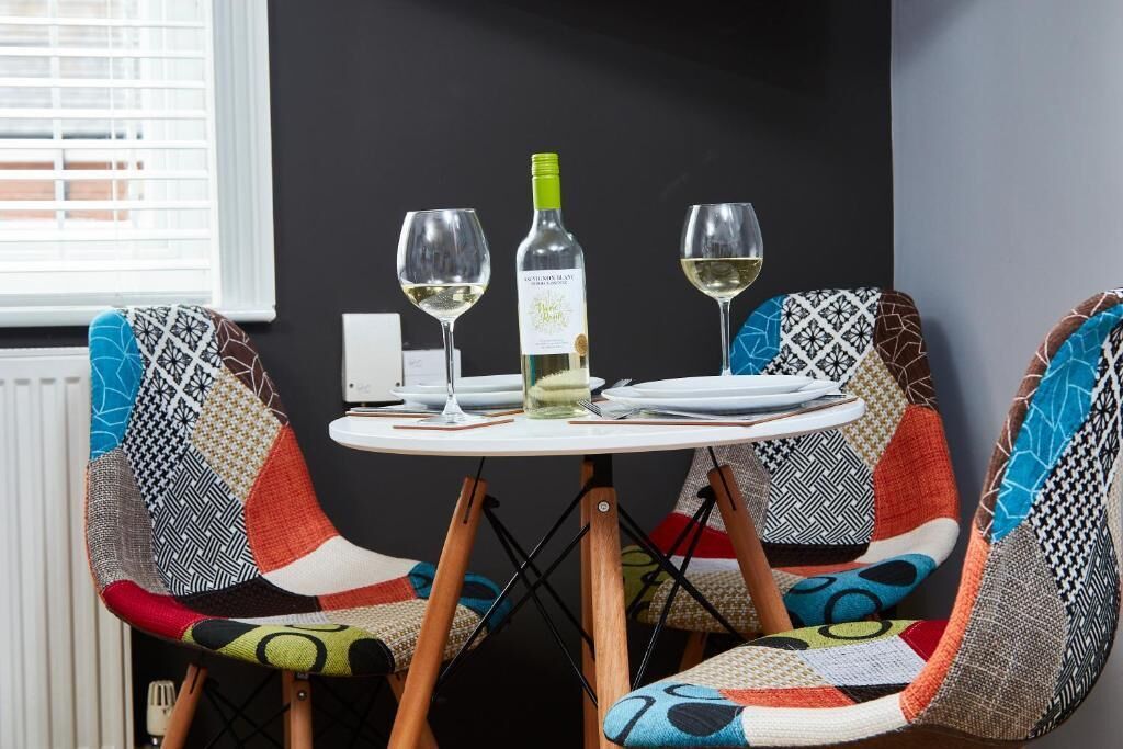 A dining table with two wine glasses and a bottle, surrounded by uniquely patterned chairs.