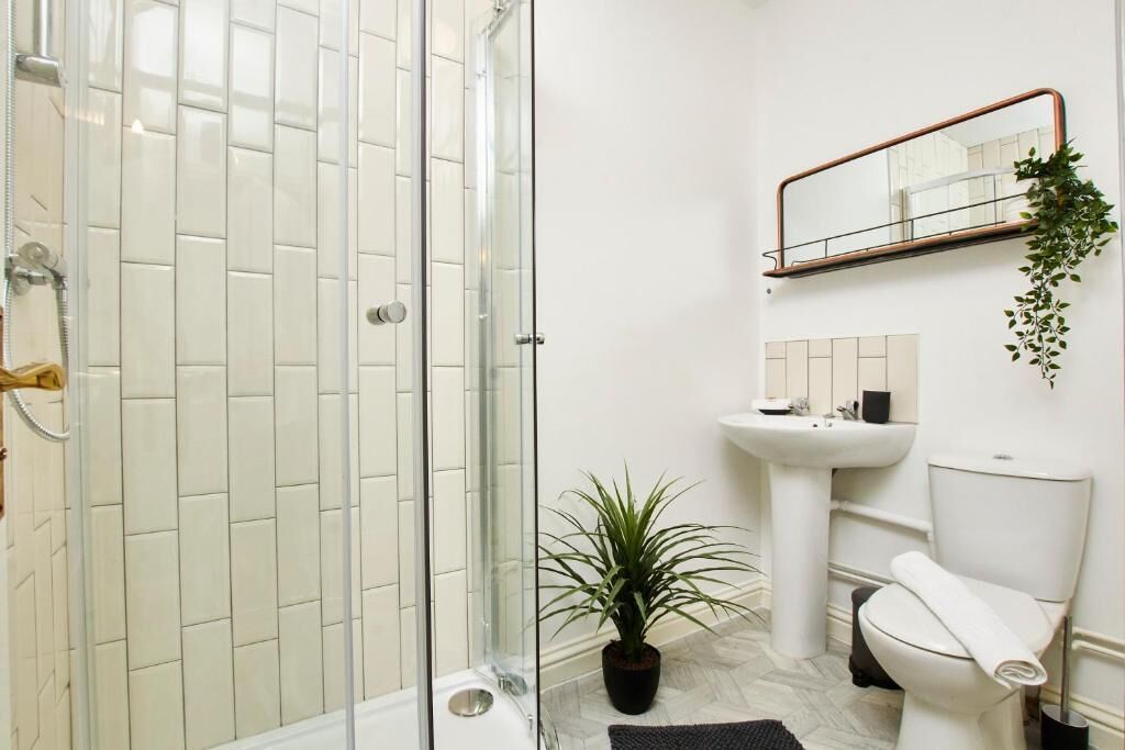 A bathroom with a glass shower enclosure, a white sink, a toilet, and a potted plant.